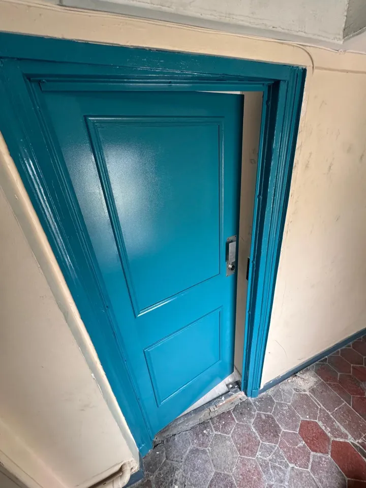 Porte palière repeinte en bleu avec serrure neuve dans un immeuble ancien
